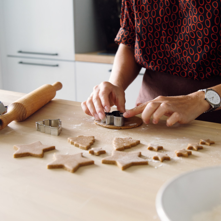 Eine Person sticht mit Formen weihnachtliche Plätzchen aus einem ausgerollten Teig.