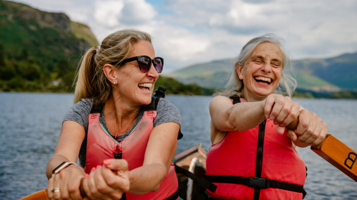 Zwei Frauen rudern zusammen über den See und lachen