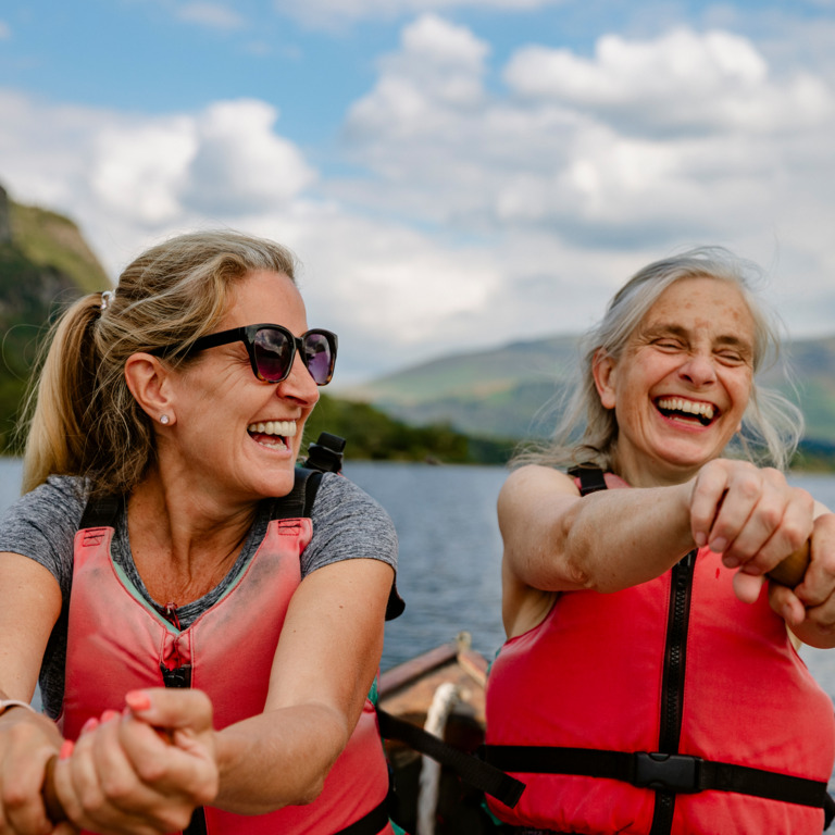 zwei Frauen mit Schwimmwesten rudern auf einem See 