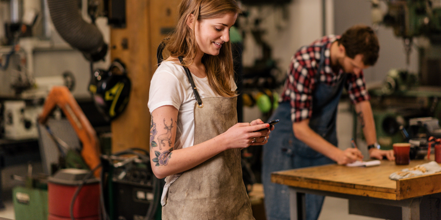 Junge Auszubildene steht in der Werkstatt und schaut auf ihr Handy