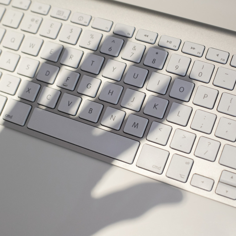 Linke Hand wirft Schatten auf PC-Tastatur.