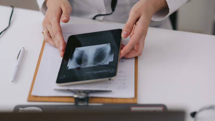 Händepaar hält ein Tablet, auf dem ein Röntgenbild zu sehen ist