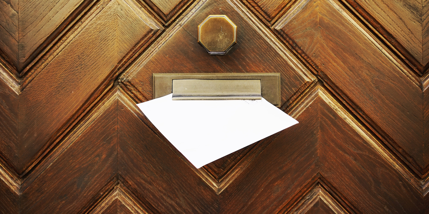 Briefumschlag mit Mitgliedsbescheinigung steckt im Briefschlitz einer Haustüre