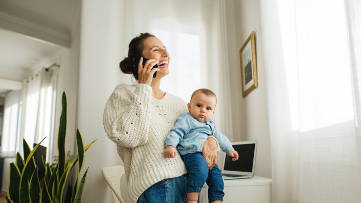 Mutter trägt Baby auf dem Arm und telefoniert mit dem Handy