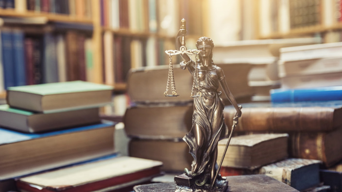 Bronzefigur Justitia steht auf einem Bücherstapel