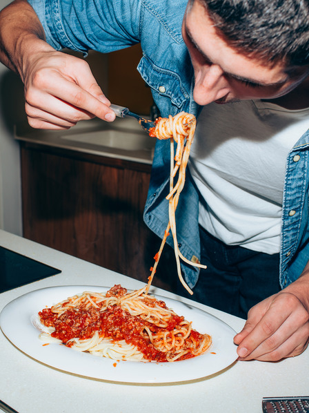 Student isst Spaghetti mit Tomatensoße im Stehen
