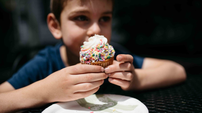 übergewichtiger Junge isst einen Muffin mit bunten Streuseln