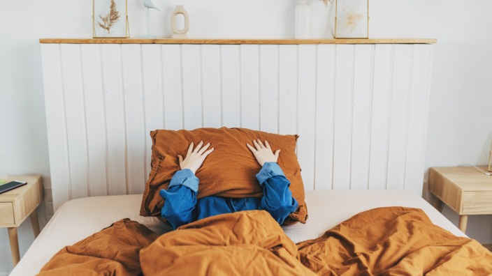 Person liegt im Bett und hält sich das Kopfkissen vor das Gesicht