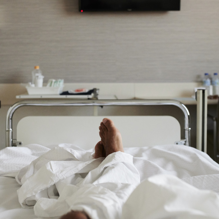 Krankenhausbett mit zwei nackten Füßen, die unter der Decke rausgucken