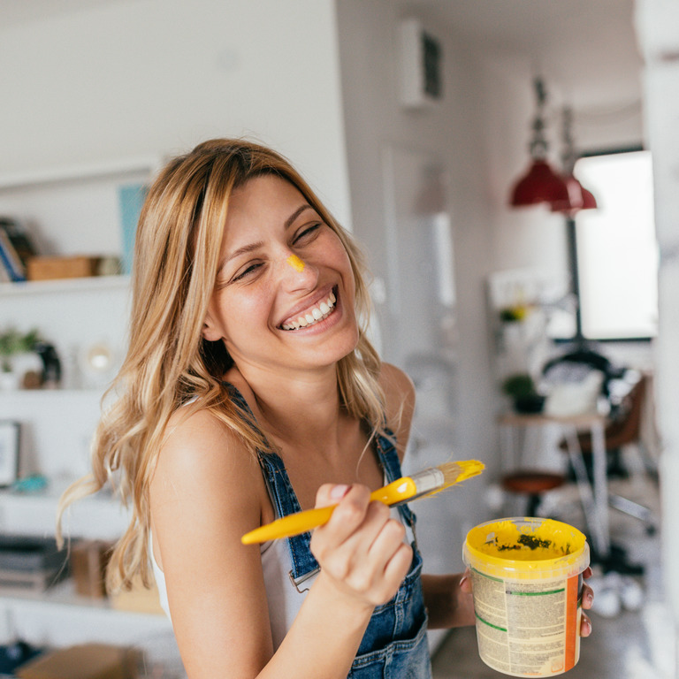 Blonde Frau malt glücklich mit gelber Farbe zuhause.