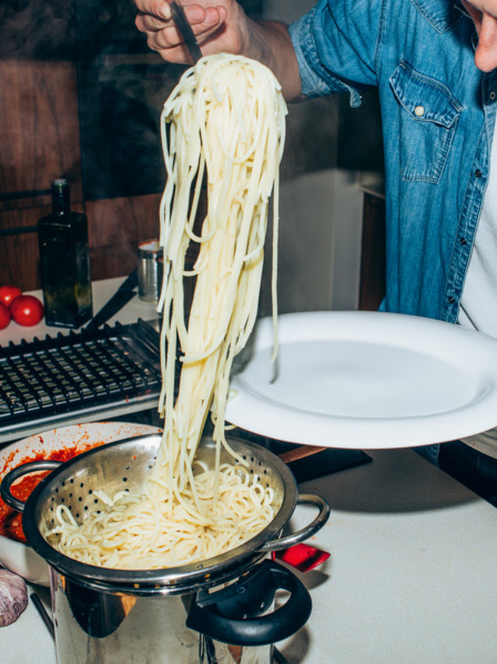 Student nimmt sich eine große Portion Spaghetti aus einem Kochtopf