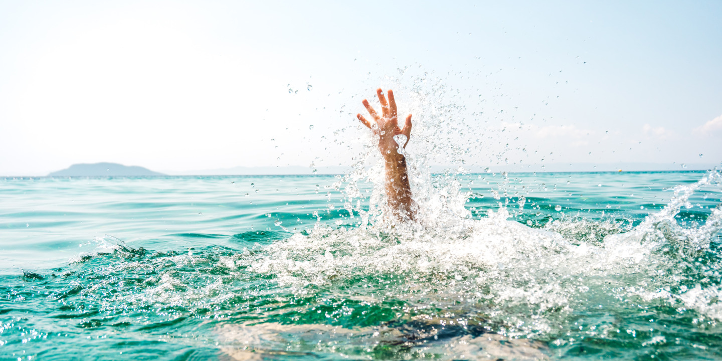 Eine schwimmende Person, die zu Ertrinken droht, streckt den Arm aus dem Wasser. 
