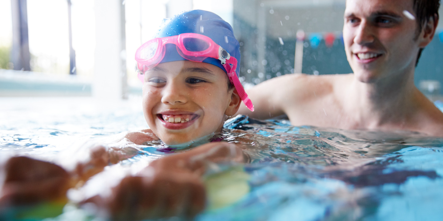 Kind lernt mit Vater schwimmen in der Schwimmhalle