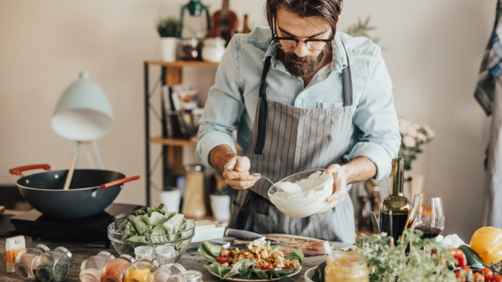 Mann träufelt selbst gemachtes Dressing über einen Teller Salat