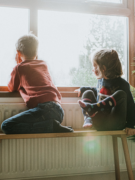 Kinder sitzen in Wohnung an der Heizung und schauen aus dem Fenster