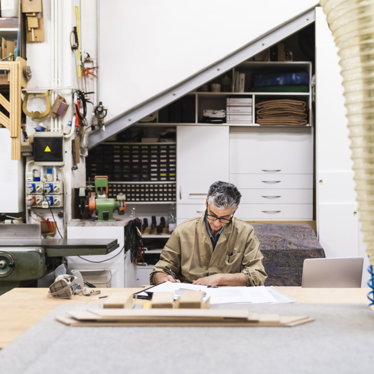 Ein Mann sitzt in Arbeitskleidung in einer Werkstatt an einem Tisch.