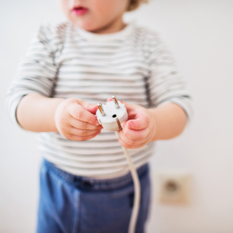 Kleinkind hält den Stecker eines Elektrogerätes in der Hand