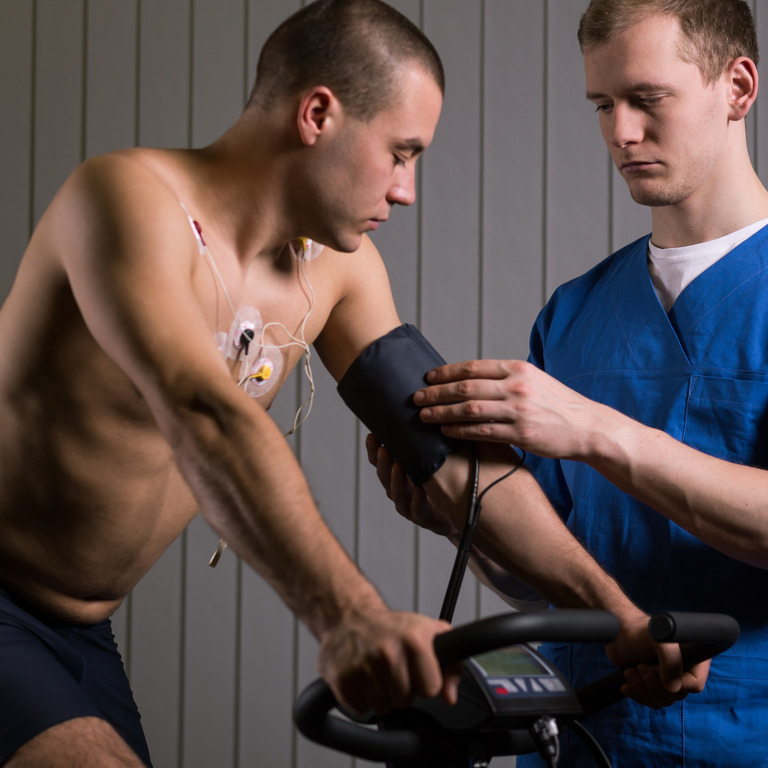 Mann mit Elektroden auf dem nackten Oberkörper macht einen Belastungstest auf dem Fahrrad