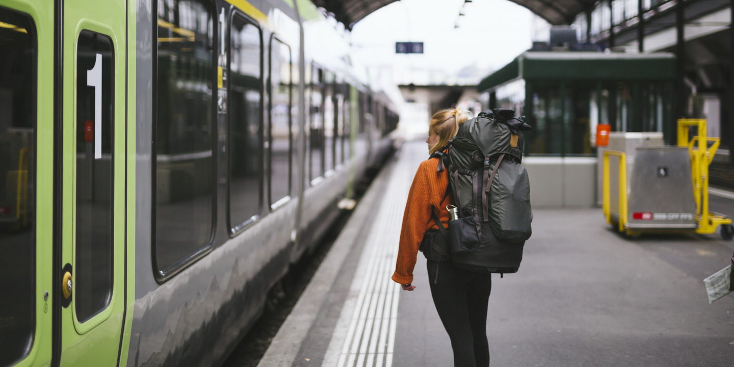 Backpackerin steht am Gleis im Bahnhof