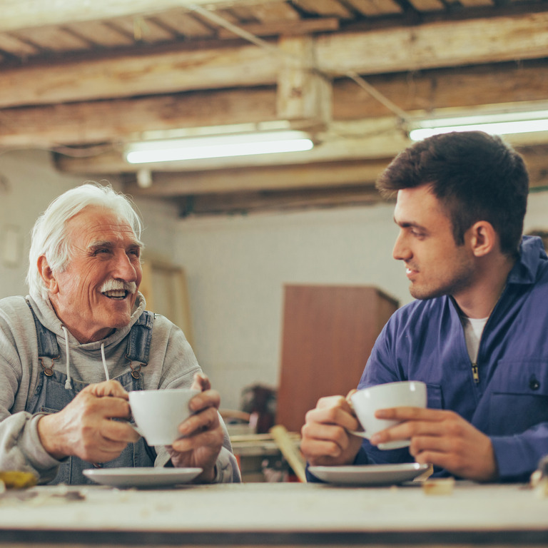 Älterer Mann und junger Mann trinken Kaffee in einer Werkstatt.