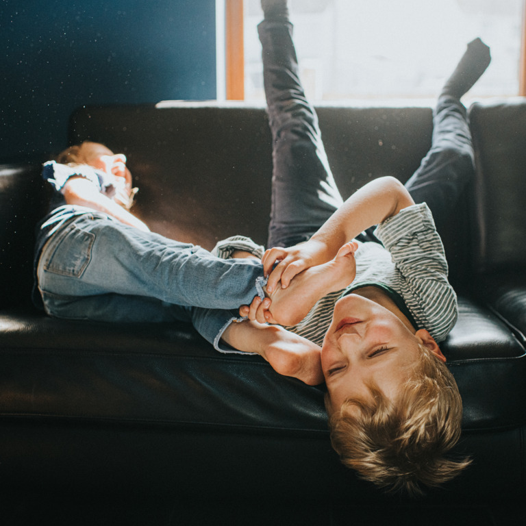 Zwei Kinder liegen auf Sofa und rangeln miteinander