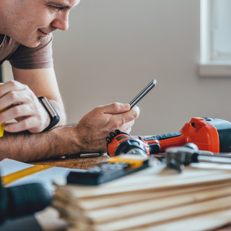 Handwerker an der Werkbank schaut aufs Smartphone.