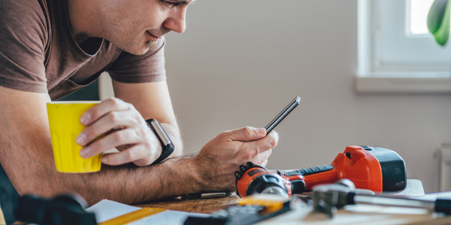 Junger Mann lehnt mit Handy in der Hand auf Arbeitspult