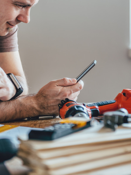 Handwerker schaut auf sein Handy und trinkt Kaffee.