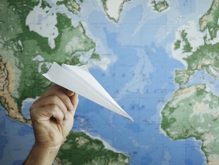 Papierflieger fliegt vor einer Weltkarte