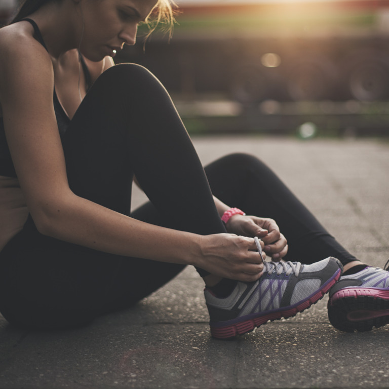 Junge Frau in Sportkleidung sitzt auf dem Boden und schnürt sich die Laufschuhe zu