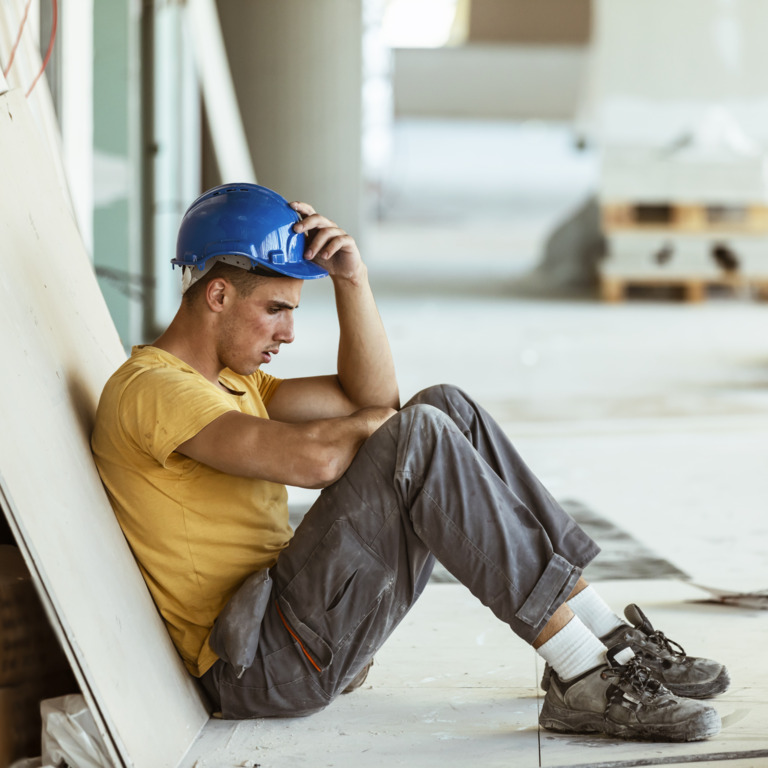 Junger Handwerker sitzt niedergeschlagen am Boden