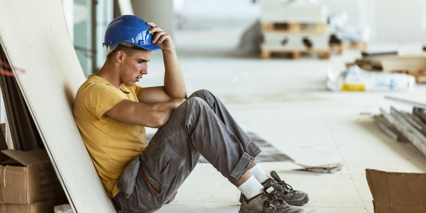 Handwerker mit Burnout sitzt niedergeschlagen am Boden