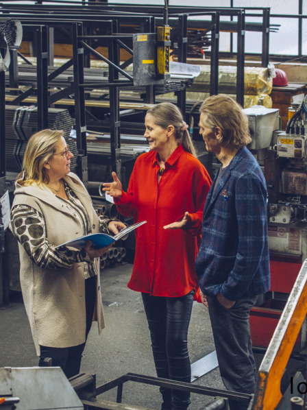 Unternehmerpaar spricht mit Mitarbeiterin in Werkshalle