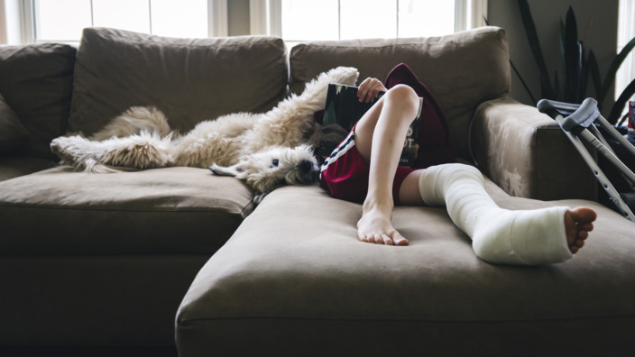 Teenager liegt mit eingegipstem Bein auf einer Couch