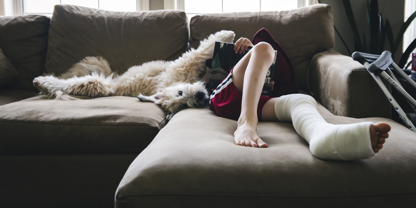 Teenager liegt mit eingegipstem Bein auf einer Couch.