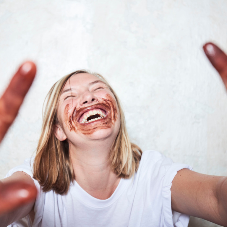 Lachende Frau mit schoko-verschmierten Händen und Mund