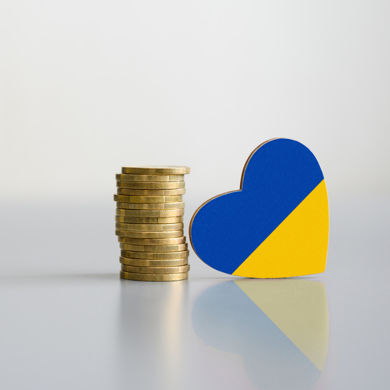 Ein Stapel Münzen und die Flagge der Ukraine in Form eines Herzens