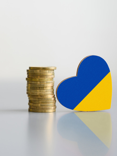 Ein Stapel Münzen und die Flagge der Ukraine in Form eines Herzens