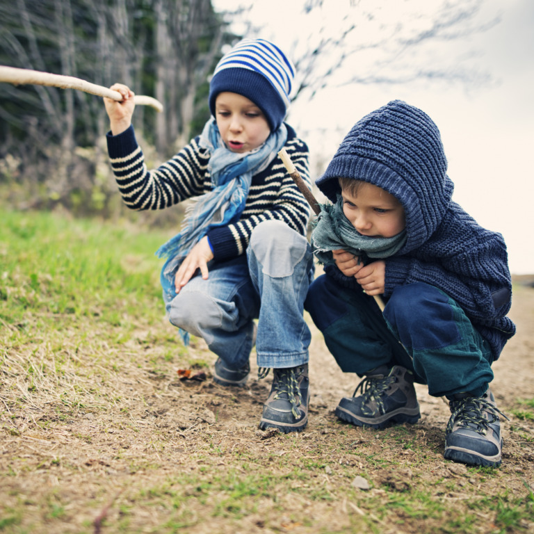 zwei Jungen hocken auf dem Boden eines Feldweges und suchen etwas