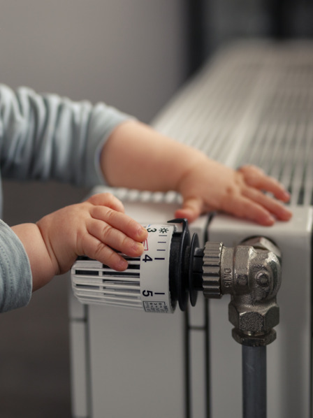 Kind spielt mit dem Thermostat des Heizkörpers