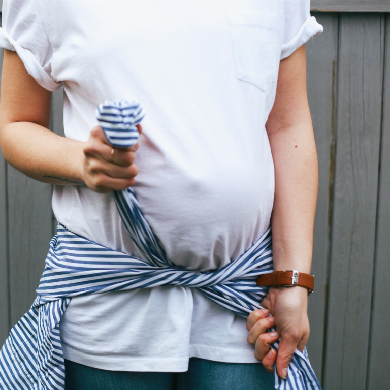 Schwangere knotet sich ein blau-weiß-gestreiftes Hemd unter ihrem Bauch um die Hüften