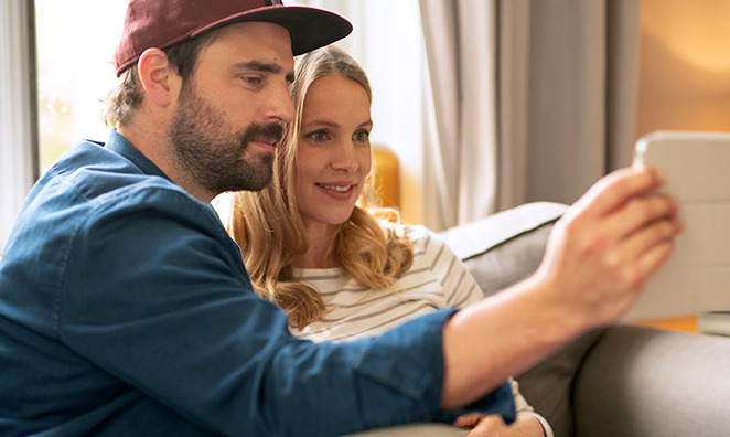 Junges Paar sitzt auf dem Sofa und schaut auf ein Tablet