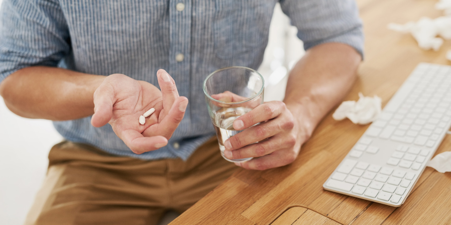 Mann mit zwei Pillen in der einen und einem Glas Wasser in der anderen Hand. 