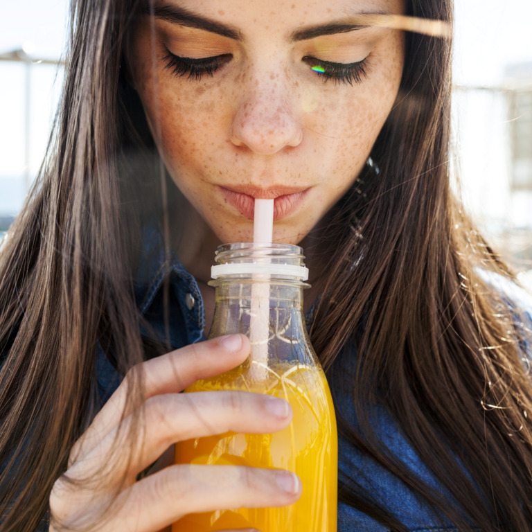 junge Frau trinkt ein isotonisches Getränk mit einem Strohhalm aus einer Flasche