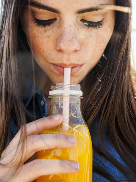 junge Frau trinkt ein isotonisches Getränk mit einem Strohhalm aus einer Flasche