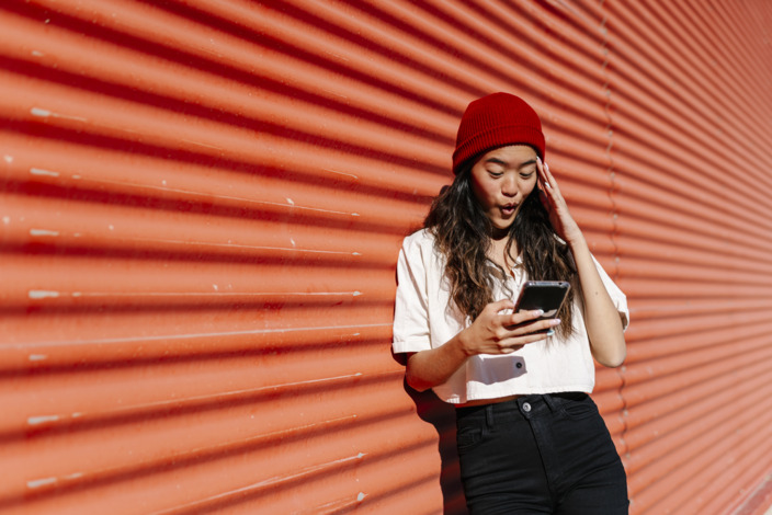 Junge Frau schaut erstaunt in ihr Smartphone