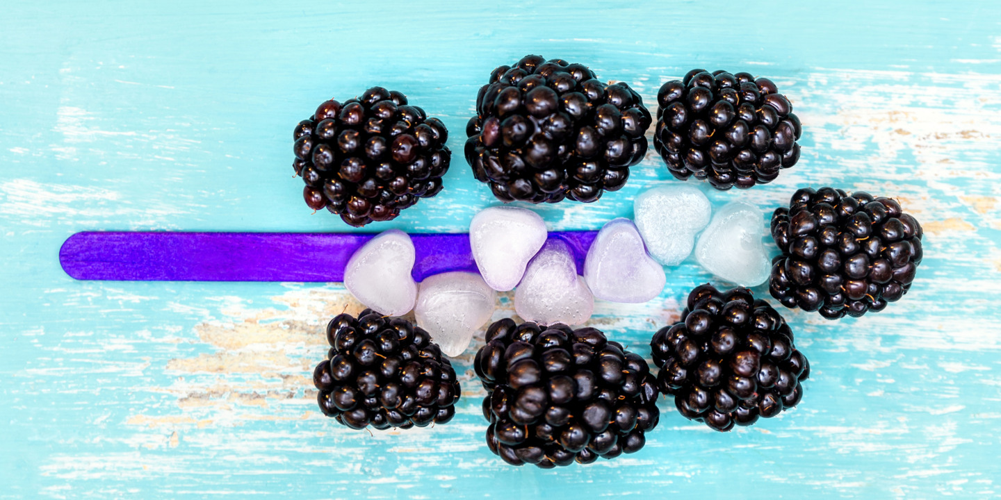 Symbolbild von Stieleis aus Brombeeren, lila Stiel und Eiswürfel in Herzform