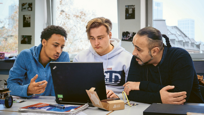 Zwei Auszubildene sitzen mit ihrem Lehrer zusammen am Laptop