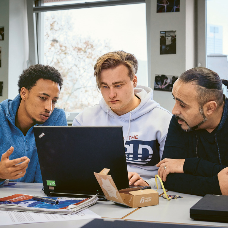 Zwei Auszubildene sitzen mit ihrem Lehrer zusammen am Laptop