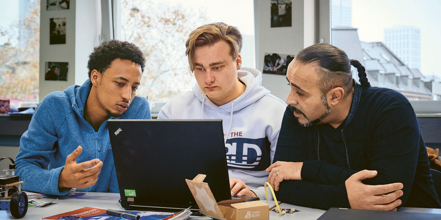 Zwei Auszubildene sitzen mit ihrem Lehrer zusammen am Laptop